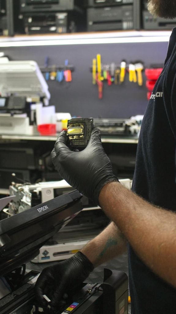 Mãos com luvas pretas de nitrilo segurando uma cabeça de impressão Epson real no laboratório